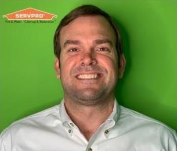 Man in button shirt in front of green background with orange logo in top left.
