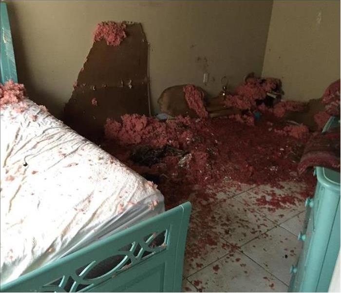 Fallen drywall and insulation on tile floor with teal bed