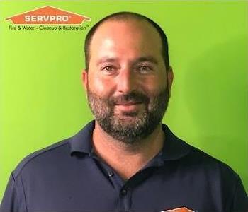Man in front of green background with orange logo in top left corner.